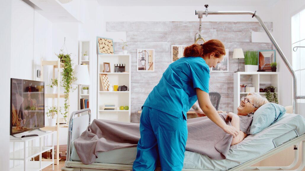 Senior woman lying in home hospital bed with a caregiver