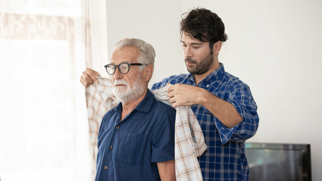 Adult son helping his elderly father get dressed