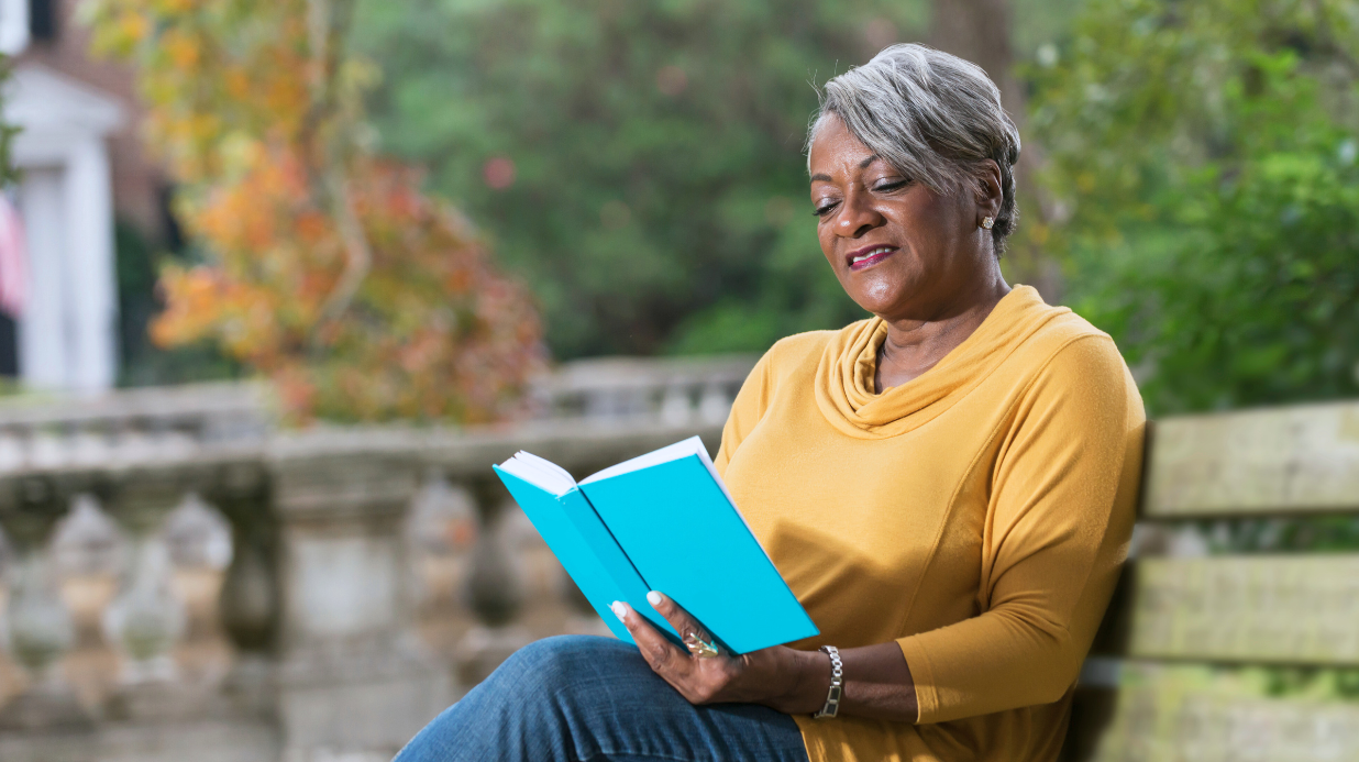 African American woman reading a book outside on a picnic bench