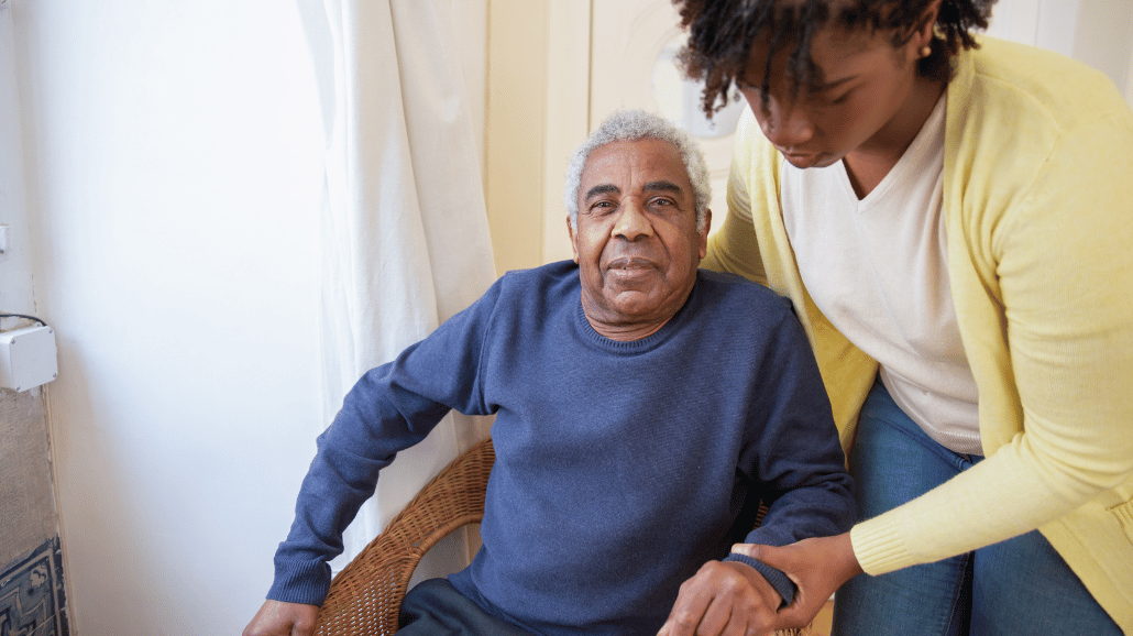 Black woman helping her dad with dementia get out of a chair