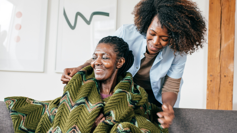 Caregiver putting an afghan around an elderly woman