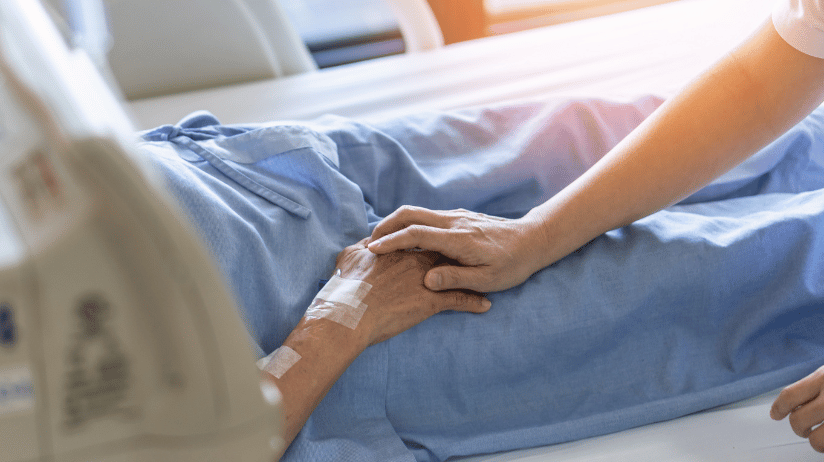 Caregiving putting her hand on a senior's hand in the hospital