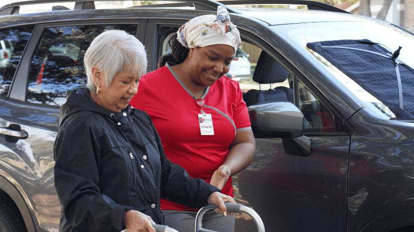 Caring Senior Service caregiver helping a senior woman walk from the car into the house