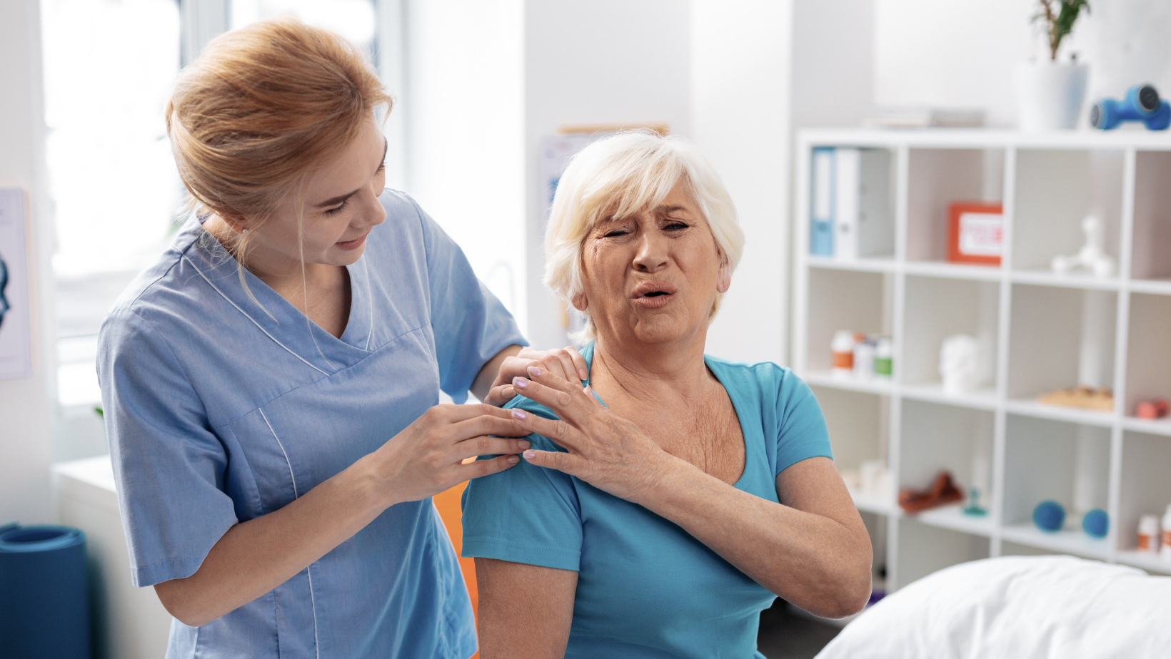 Caregiver helping a senior woman who is grimacing with shoulder pain