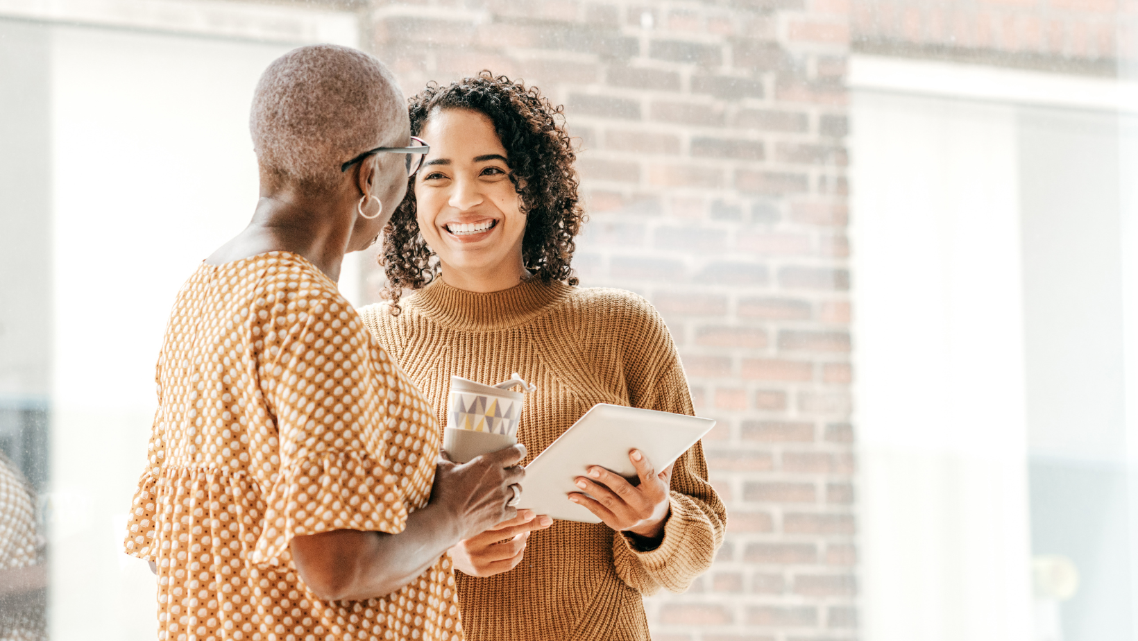 Two professional women talking in an office with exposed brick walls