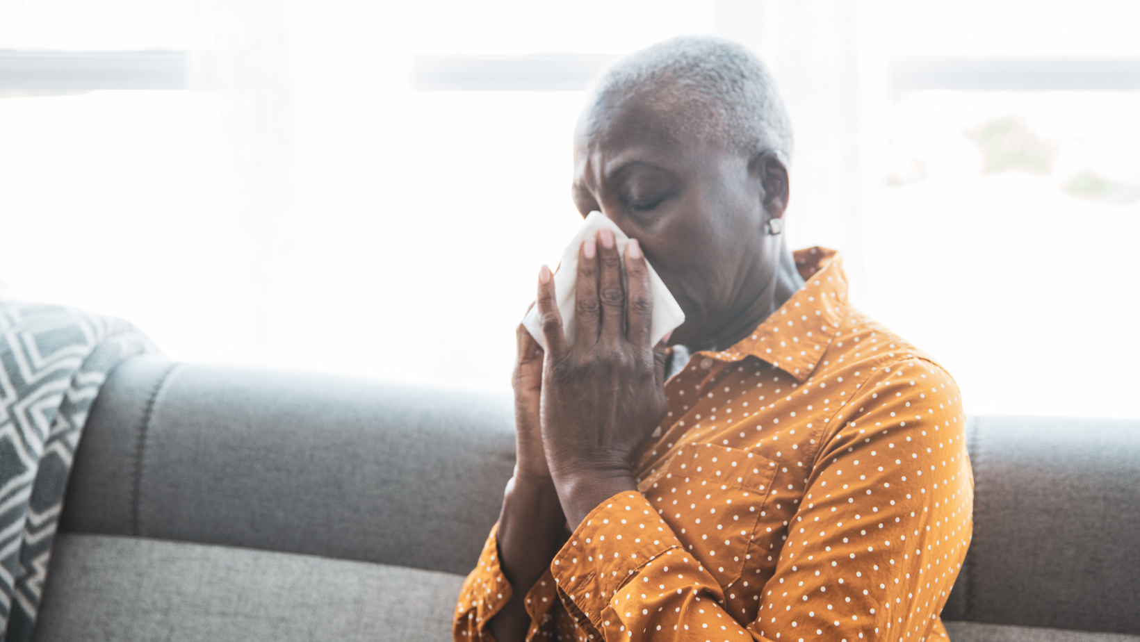 Blog20Covers20286929 Black senior woman sitting on a couch and blowing her nose