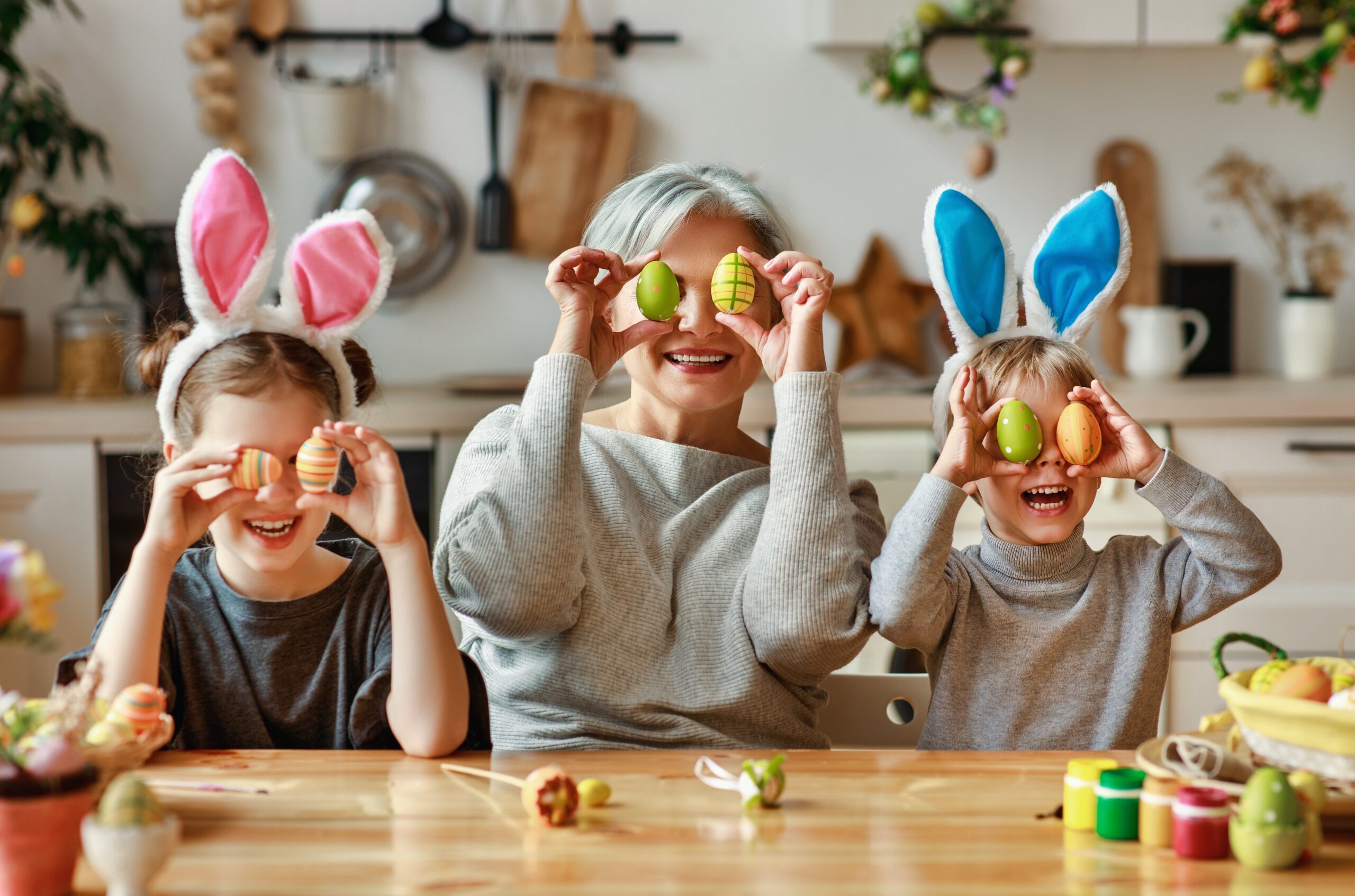Grandma with grandkids wearing bunny ears and holding up Easter eggs