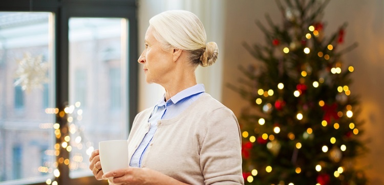 Lonely senior looking out the window with a Christmas tree in the background