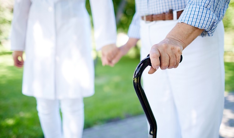 Senior using a cane one a walk with caregiver
