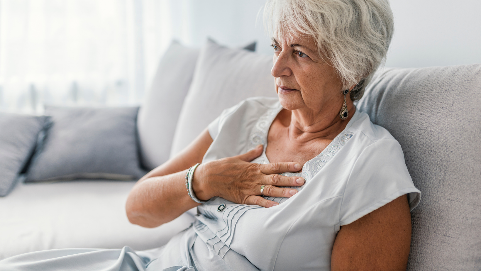 Untitled20design20-202022-02-09T133515.119 Senior woman holding her chest while sitting on a couch