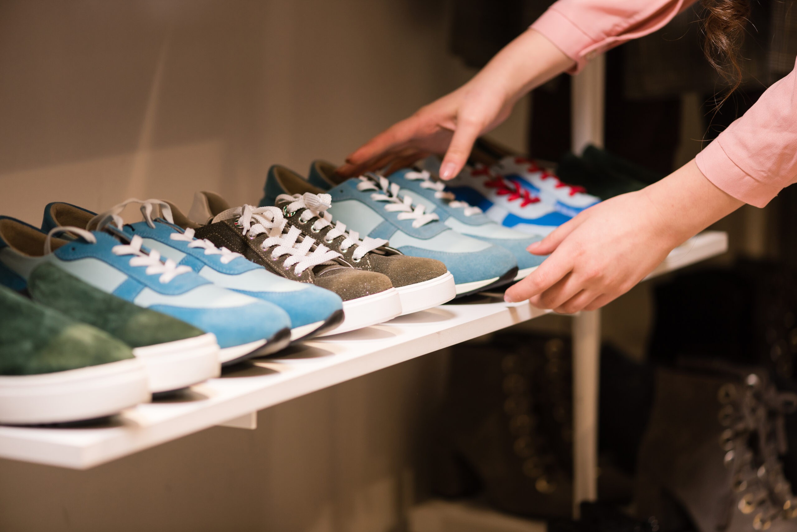 Woman puts sneakers collection on store rack.