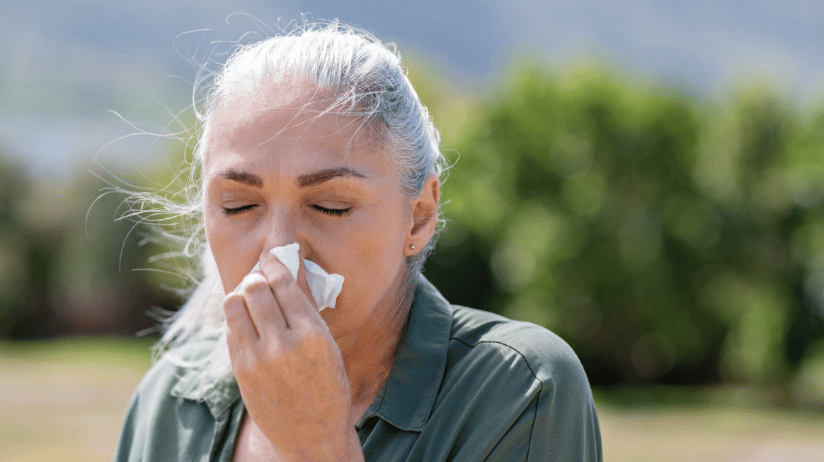 Senior woman outdoors blowing her nose