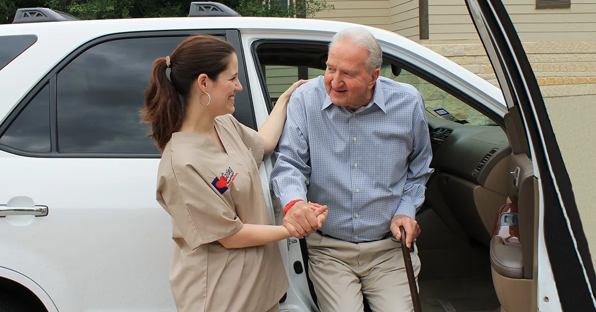 Caregiver assisting older man with stepping out of a vehicle