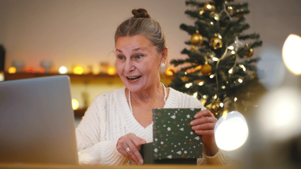 Senior woman unwrapping a Christmas gift while in front of a laptop