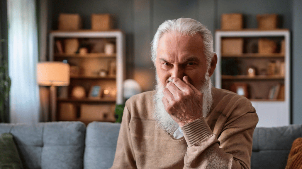 Old man sitting on a couch covering his nose because of a bad smell