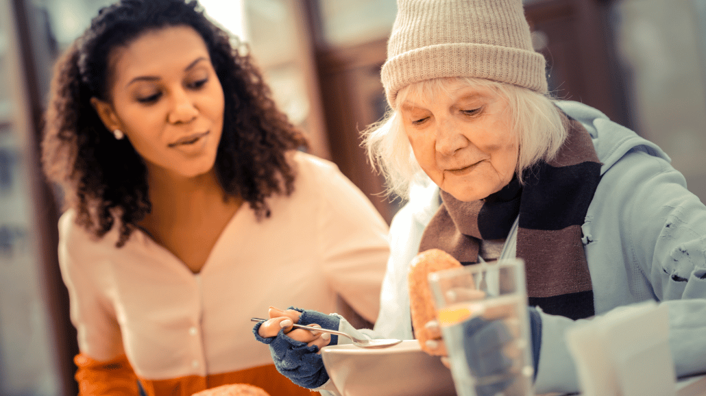 Young woman feeding a homeless senior woman