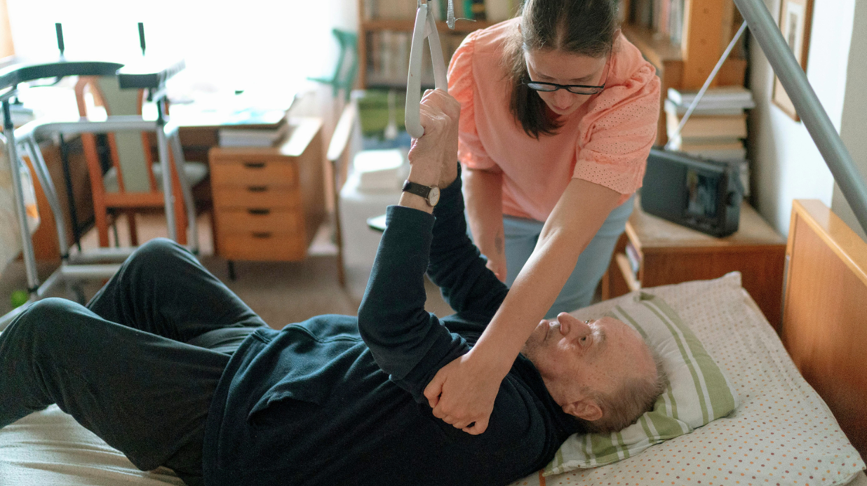 Veteran receiving help with physical therapy in bed from a family caregiver