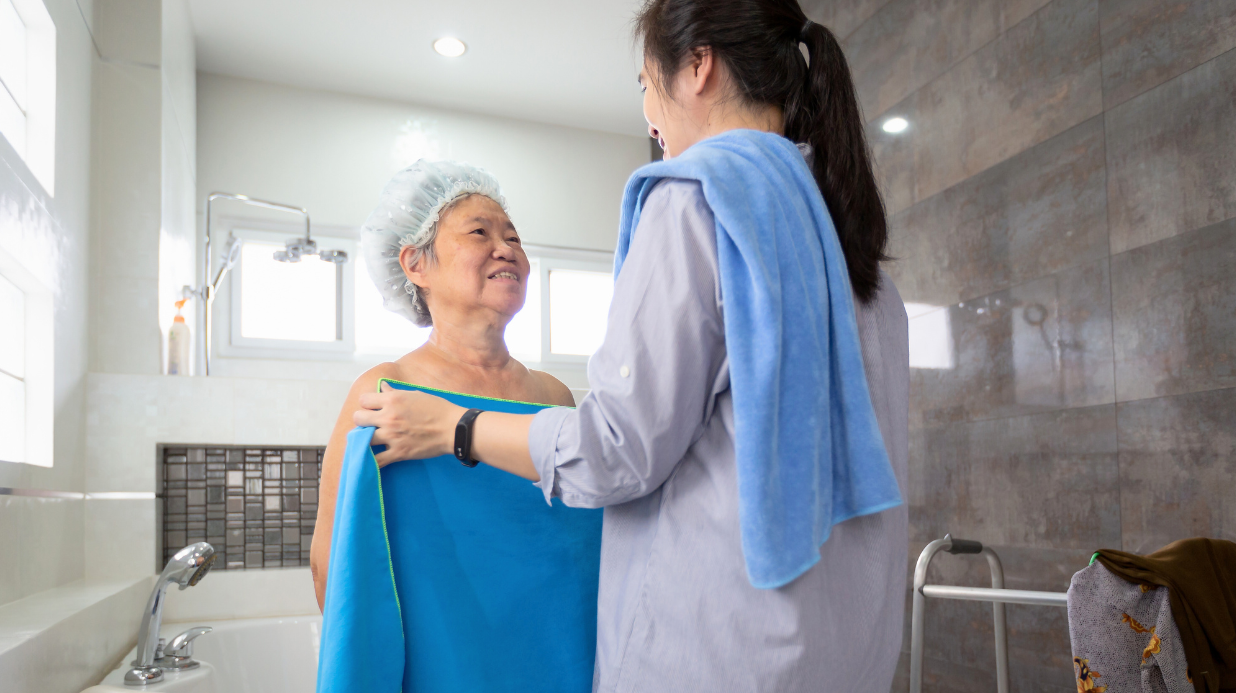 Asian daughter or female care assistant help her senior mother wipe her body after shower in bathroom at home