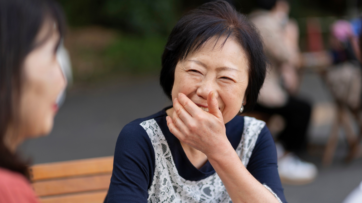 Senior woman sitting outside on a bench with a friend while laughing