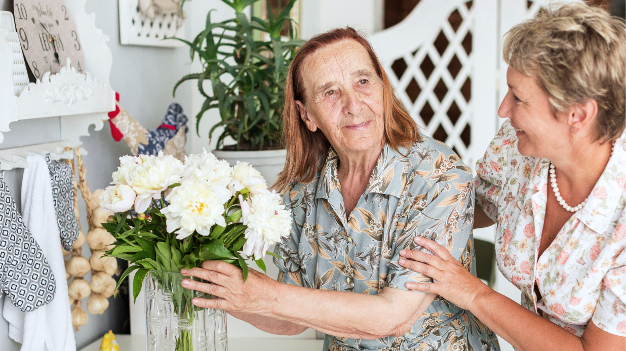 Senior woman holding a vase of white flowers while standing by her adult daughter